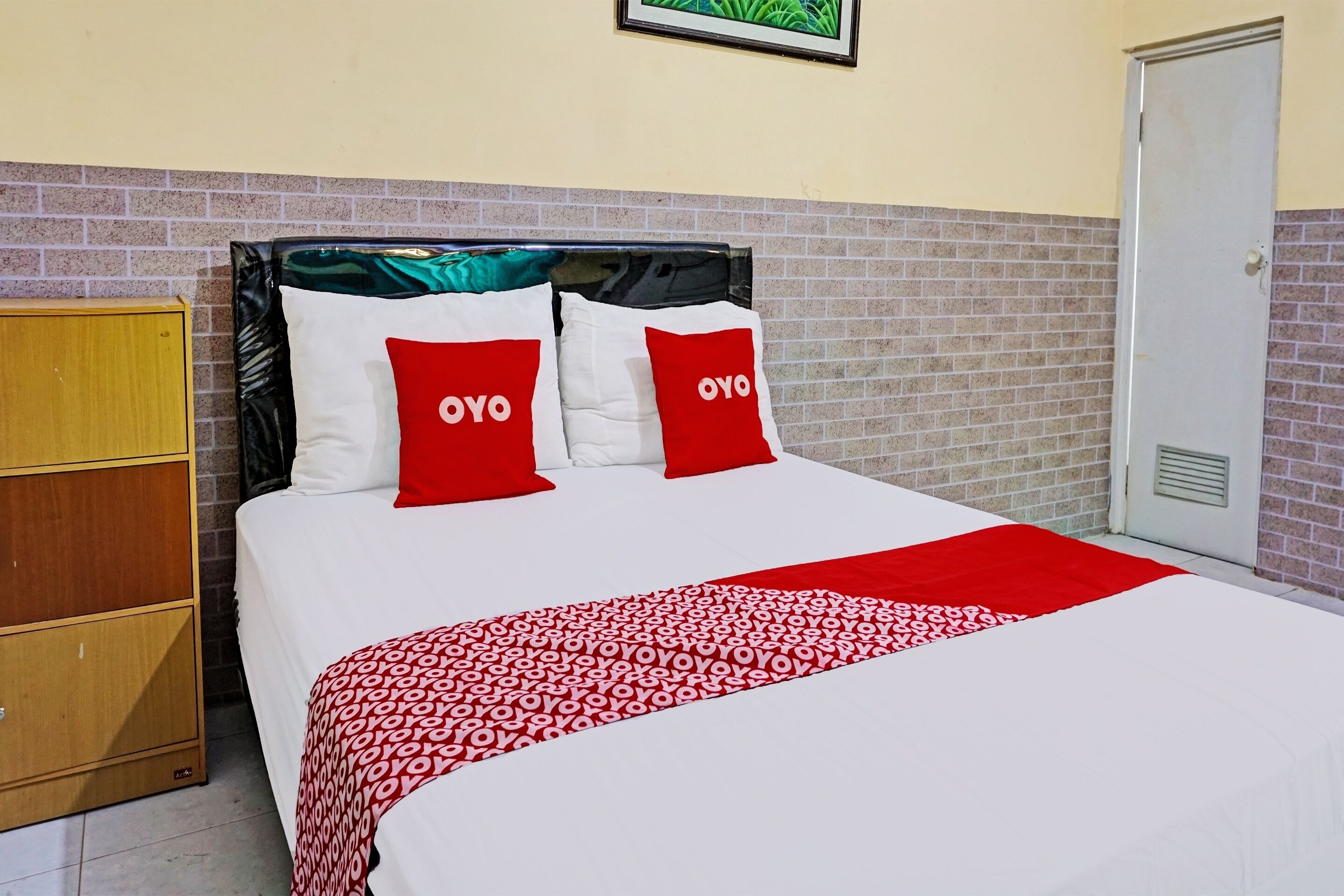 Cama bem arrumada com colcha estampada em vermelho e branco e duas almofadas vermelhas com a inscrição 'OYO'.