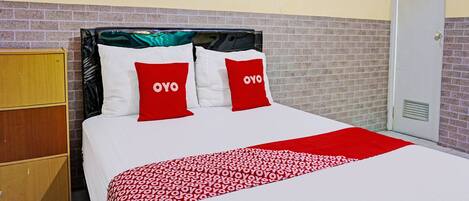 Cama bem arrumada com colcha estampada em vermelho e branco e duas almofadas vermelhas com a inscrição 'OYO'.