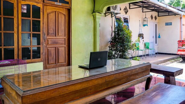 A wooden table with a laptop, a bench, and a green wall with a door and windows. - OYO 92359 Kost Maluku 36 Family Residence (Kanigoro)