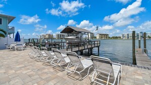 A waterfront patio with lounge chairs, a covered seating area, and a view of the marina and city skyline. - Enchanted Inn Suite #6: Waterfront, Pool, Fishing Dock, Boat Docks & Tiki Bar! (Clearwater)