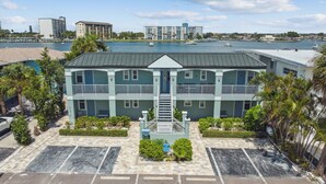 A two-story hotel with a central staircase, a parking lot, and a marina in the background. - Enchanted Inn Suite #6: Waterfront, Pool, Fishing Dock, Boat Docks & Tiki Bar! (Clearwater)