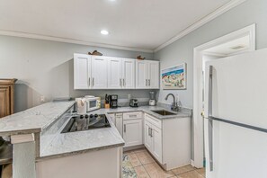 A kitchen with white cabinets, a microwave, a stove, a sink, and a refrigerator.