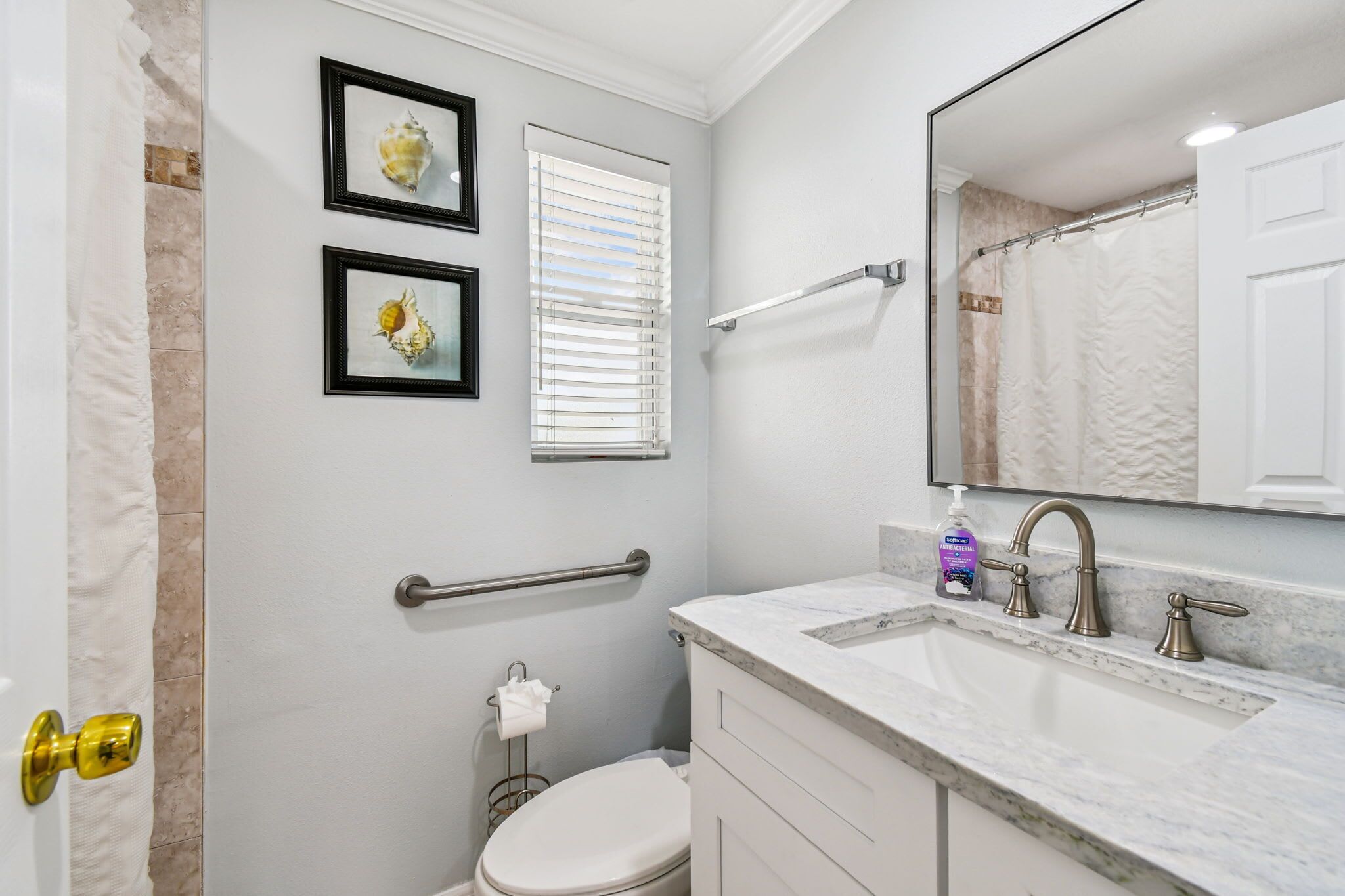 A bathroom with a white toilet, a sink with a marble countertop, a large mirror, and two framed pictures on the wall.