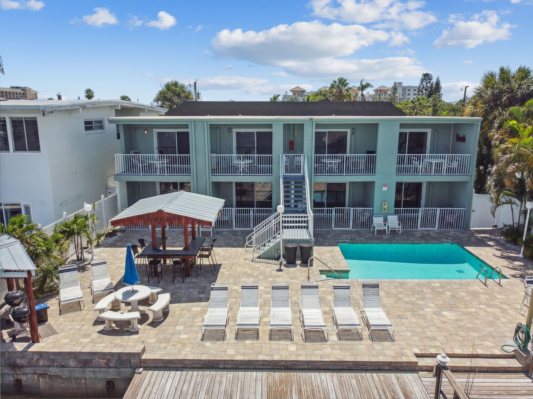 Un hotel de varios pisos con piscina, mobiliario exterior y terraza de madera.