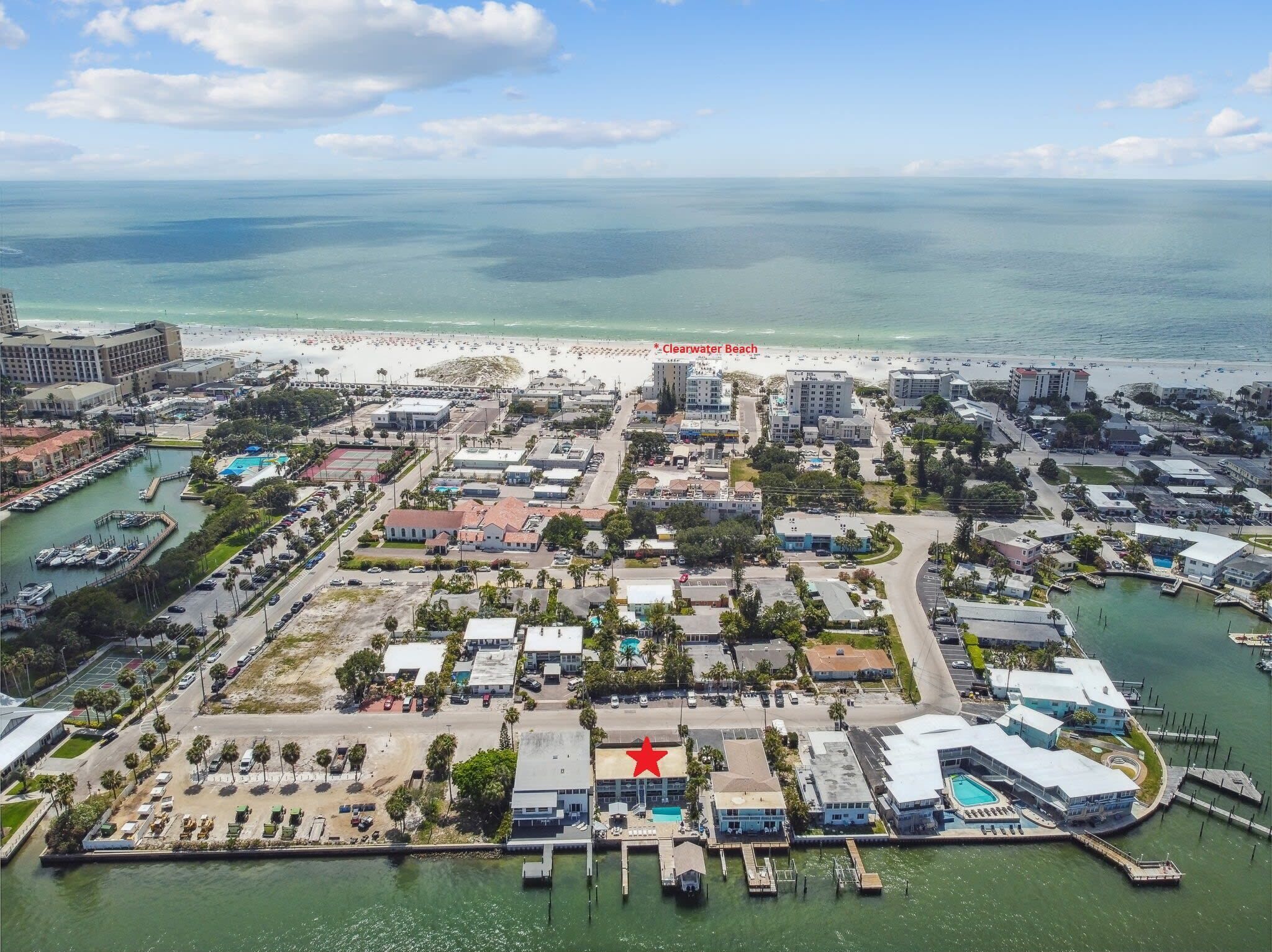 An aerial view of a coastal town with a marina, beach, and various buildings.