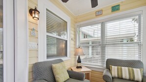 A cozy room with two patterned armchairs, a small table with a lamp, and a window with blinds. - Beachside Cottage 22 Steps to Beach | Beach Gear Included! (Clearwater)