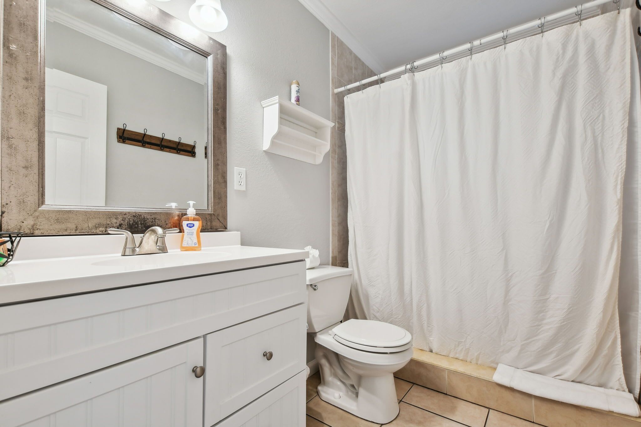 Une salle de bain avec un lavabo blanc, un miroir, des toilettes et un rideau de douche.