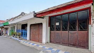 A street view with a building featuring a closed metal gate, a blue fence, and potted plants.