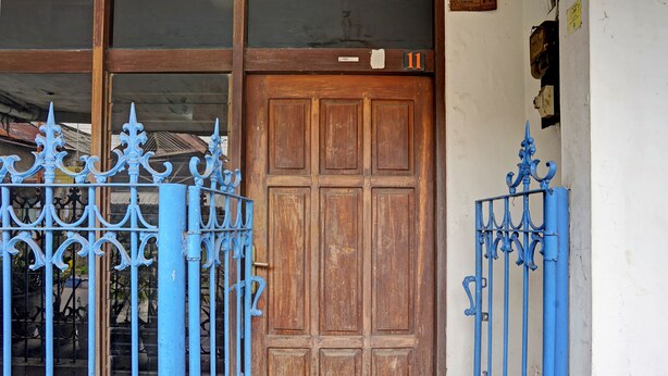 Una puerta de madera con una placa numérica, flanqueada por elaboradas rejas azules.