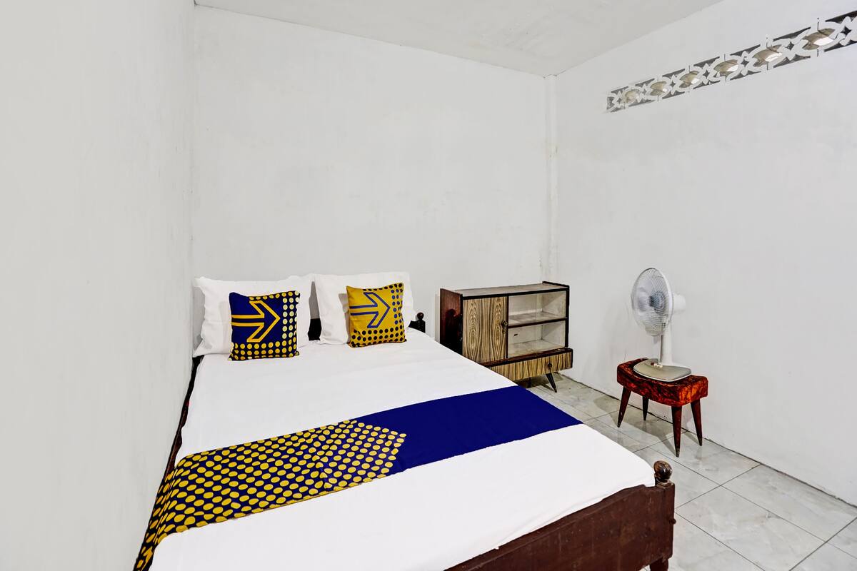 A bedroom with a bed, pillows, a wooden cabinet, and a standing fan.