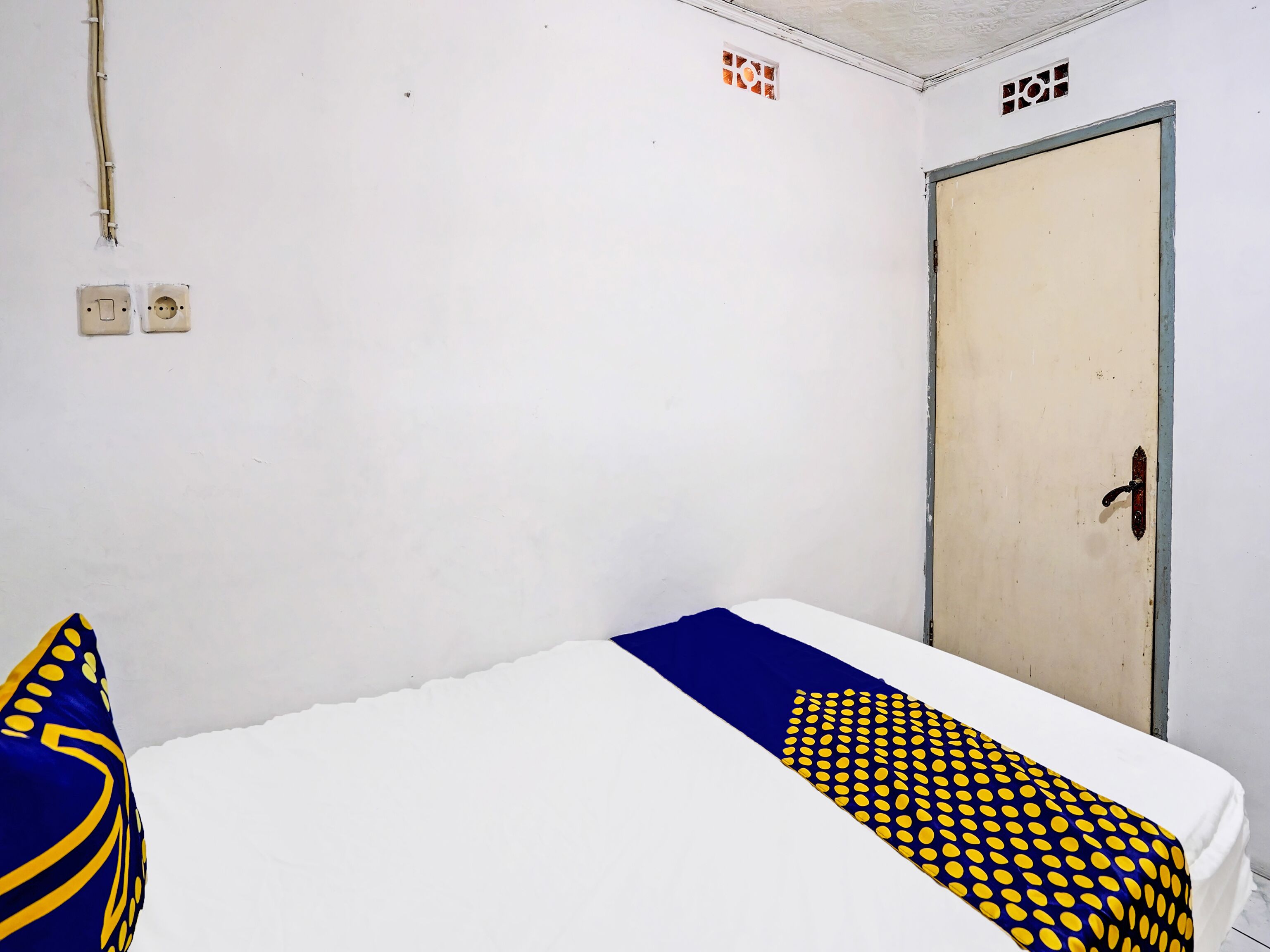 A room with a bed, a door, and a wall socket.