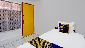Una habitación de hotel con una cama, un almohadón de diseño geométrico, una puerta amarilla y cortinas estampadas.