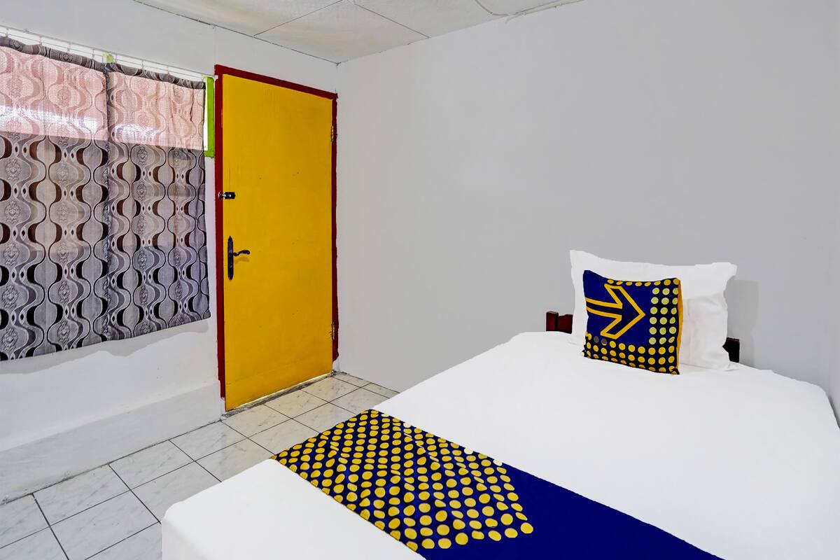 A hotel room with a bed, a pillow with a geometric pattern, a yellow door, and patterned curtains.