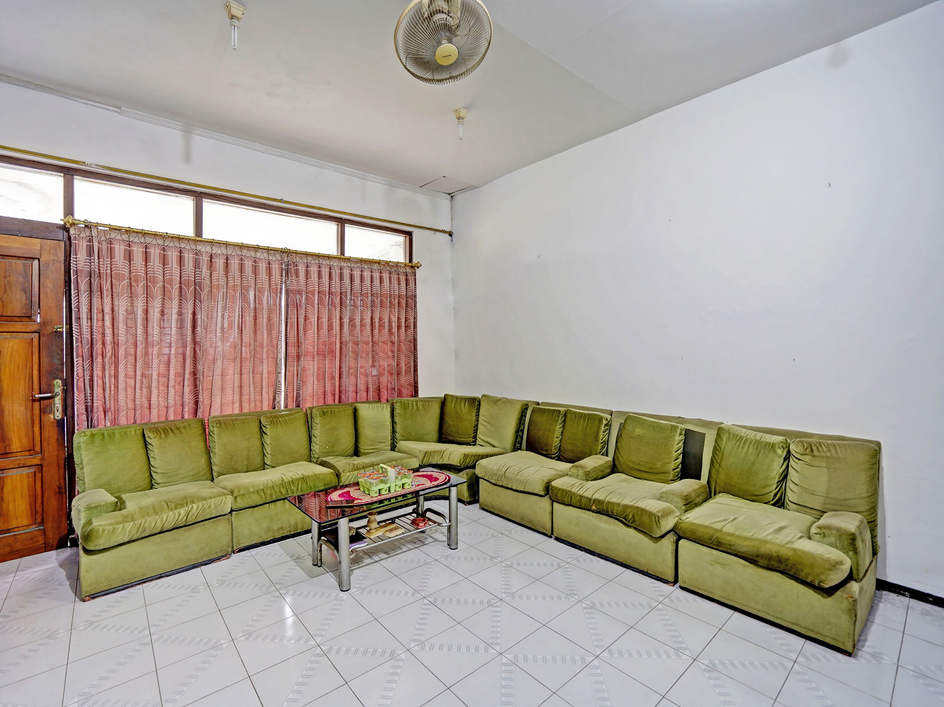 A living room with a green sectional sofa, a coffee table, and a fan.