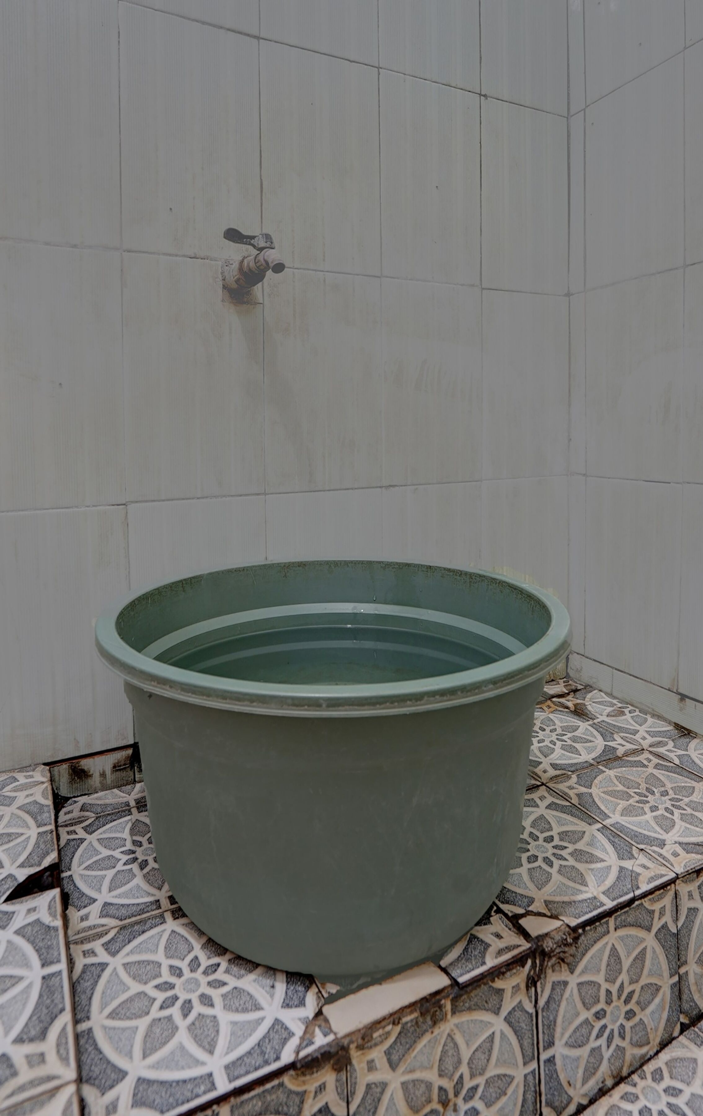 Una piscina grande y verde, circular, con un grifo en la pared de fondo, ubicada sobre un suelo de baldosas estampadas.