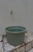 Una piscina grande y verde, circular, con un grifo en la pared de fondo, ubicada sobre un suelo de baldosas estampadas.