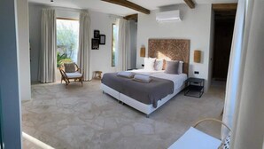 A bedroom with a large bed, a chair, a small table, and a view of greenery outside. - Villa Bamboa – Ibiza-Styled Tropical Escape Near Jan Thiel Beach (Jan Thiel)