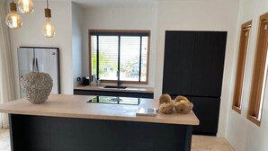 A modern kitchen with a central island, a refrigerator, and a window with blinds. - Villa Bamboa – Ibiza-Styled Tropical Escape Near Jan Thiel Beach (Jan Thiel)
