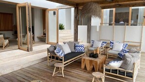 A wooden deck with a sofa set, a hanging light fixture, and a sliding glass door leading to an interior space. - Villa Bamboa – Ibiza-Styled Tropical Escape Near Jan Thiel Beach (Jan Thiel)