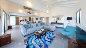 Un salón amplio con un sofá de color claro, un sillón azul y una mesa de centro.