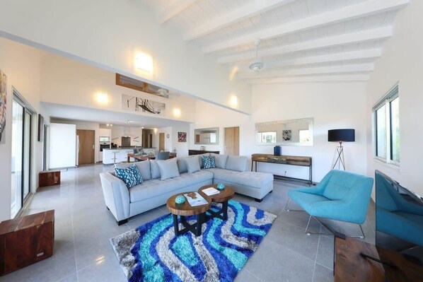 Un salón amplio con un sofá de color claro, un sillón azul y una mesa de centro.