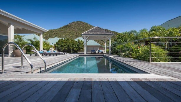 Una terraza de madera con piscina, sillas de descanso y un pabellón.