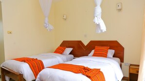 Una habitación de hotel con dos camas, cada una con ropa blanca y mantas anaranjadas a rayas. Posee cabeceros de madera y mesitas de noche a juego.