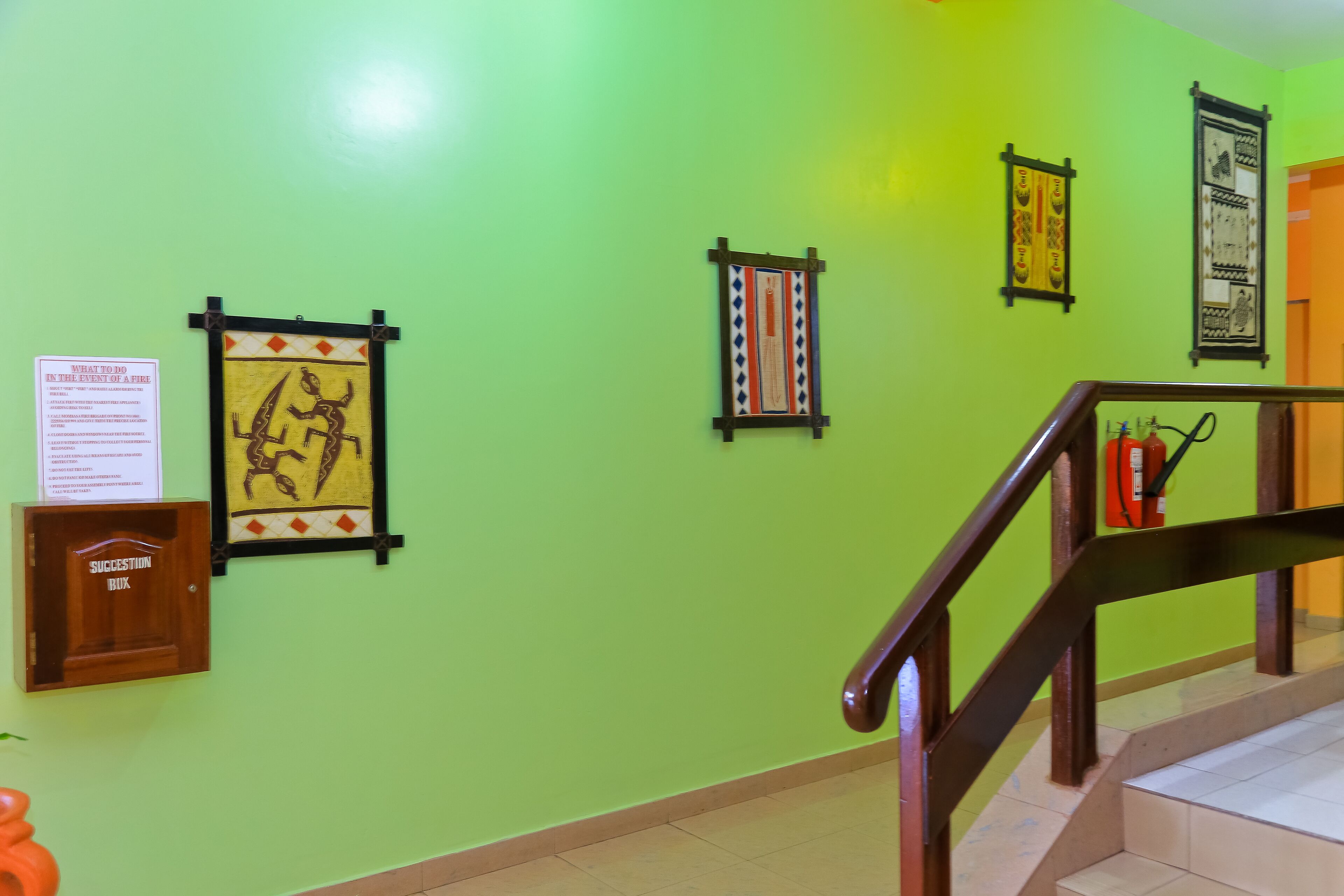 Una pared verde con cuadros enmarcados, un buzón de sugerencias de madera y una escalera con barandilla de madera.