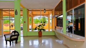 Zona de recepción con un banco, una planta en maceta y un mostrador con una computadora.