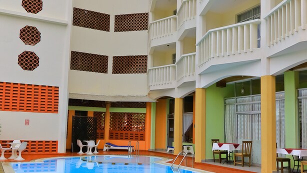 Una piscina cubierta de varios niveles con superficie de agua azul cristalina, rodeada de balcones blancos con barandillas y un área de descanso con mesas y sillas.
