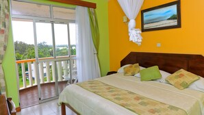 Habitación de hotel con balcón, cama con ropa de cama verde y color beige, y un cuadro de una playa.