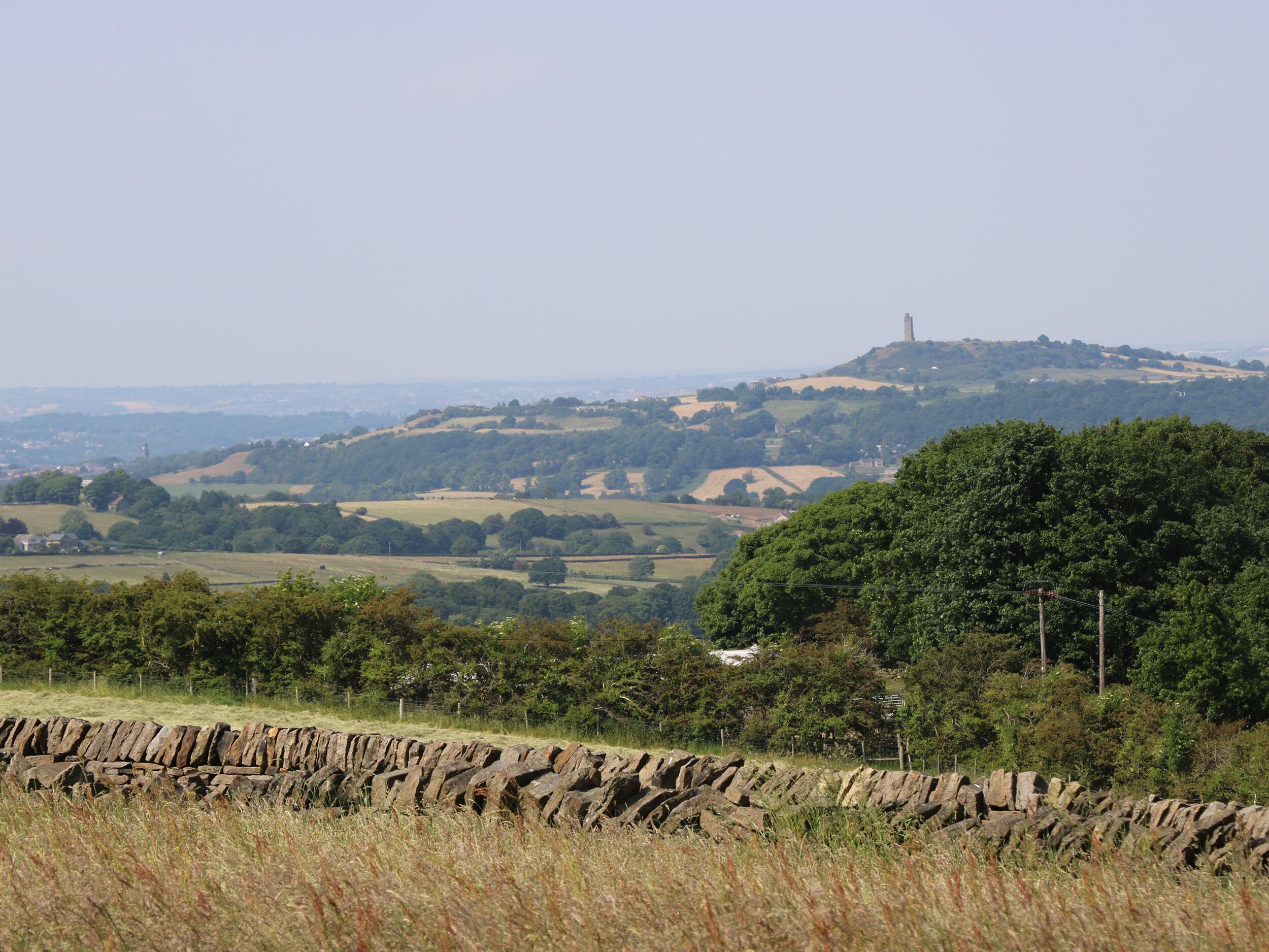 A rural landscape with rolling hills, a stone wall, and a distant tower.