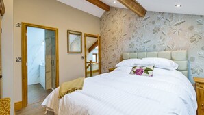 Un dormitorio con una cama grande, vigas de madera, papel tapiz floral y vistas a una escalera.