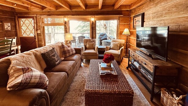 A cozy log cabin interior with a sofa, chairs, a coffee table, and a television.