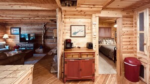 A cozy log cabin interior with a living area, kitchen, and bedroom.