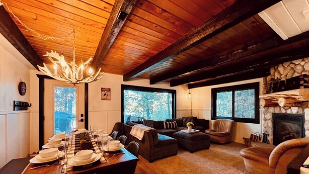 A cozy living room with a wooden ceiling, a fireplace, and a dining area set up for a meal. - Lakefront with private dock & fire pit - Bunk House Cabin (Island Park)