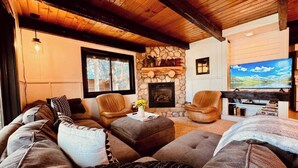 A cozy living room with a stone fireplace, leather chairs, and a television. - Lakefront with private dock & fire pit - Bunk House Cabin (Island Park)