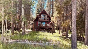 A wooden cabin with a balcony, surrounded by trees in a forest. - Lakefront with private dock & fire pit - Bunk House Cabin (Island Park)