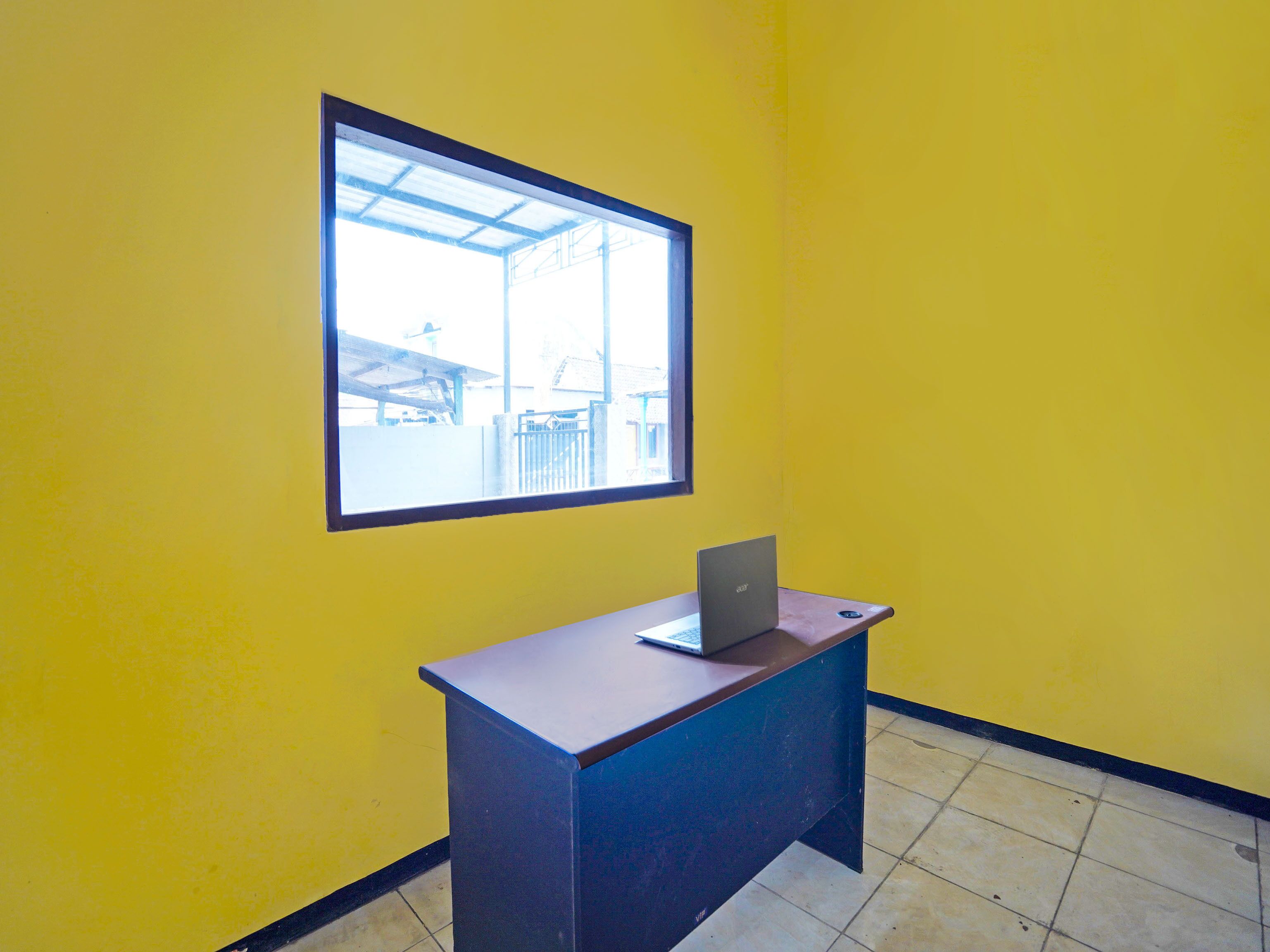 Een kamer met gele wanden, een raam en een bureau met een laptop.