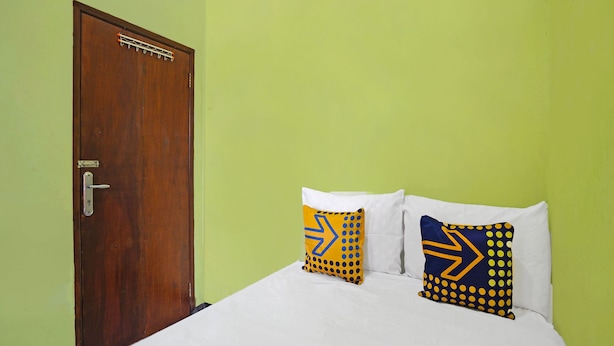 A room with a wooden door, a bed with white bedding, and two pillows with yellow and blue patterns.