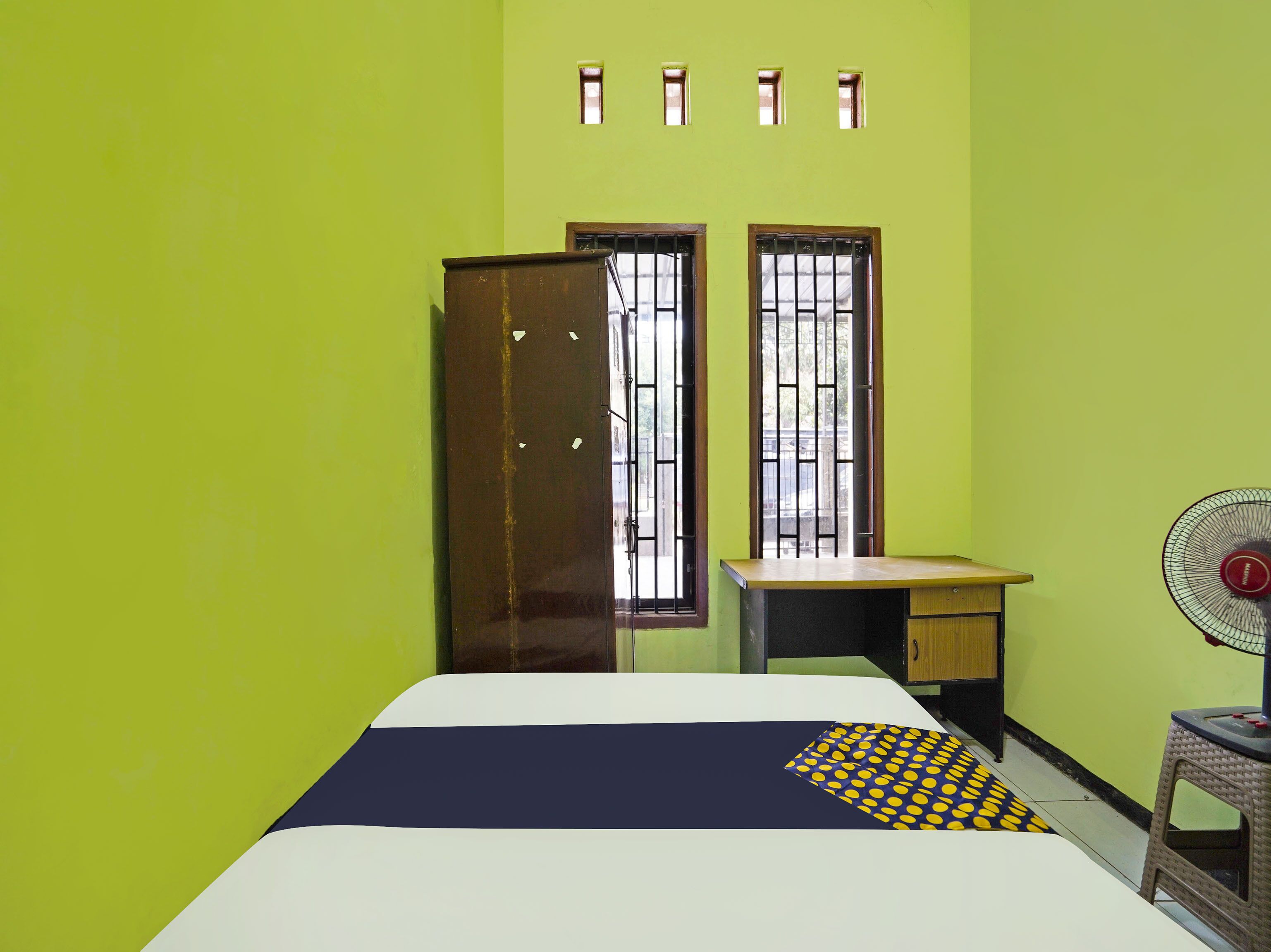 Una habitación con cama, escritorio, silla y ventilador.