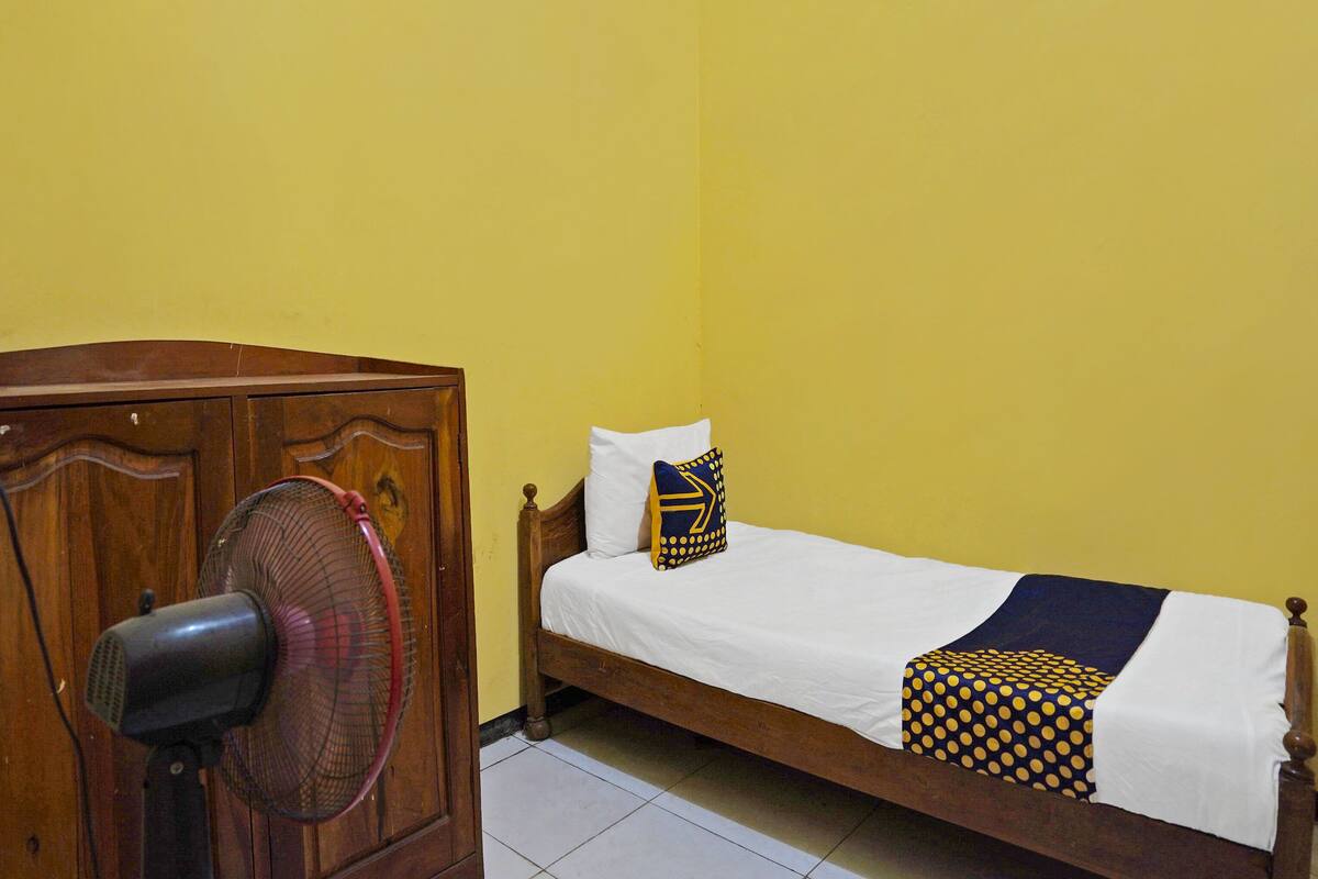 A single bed with a white sheet and two pillows, one with a geometric pattern.