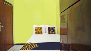 Una habitación con cama, dos almohadas estampadas con motivos de flechas, un armario de madera y suelo de baldosas.