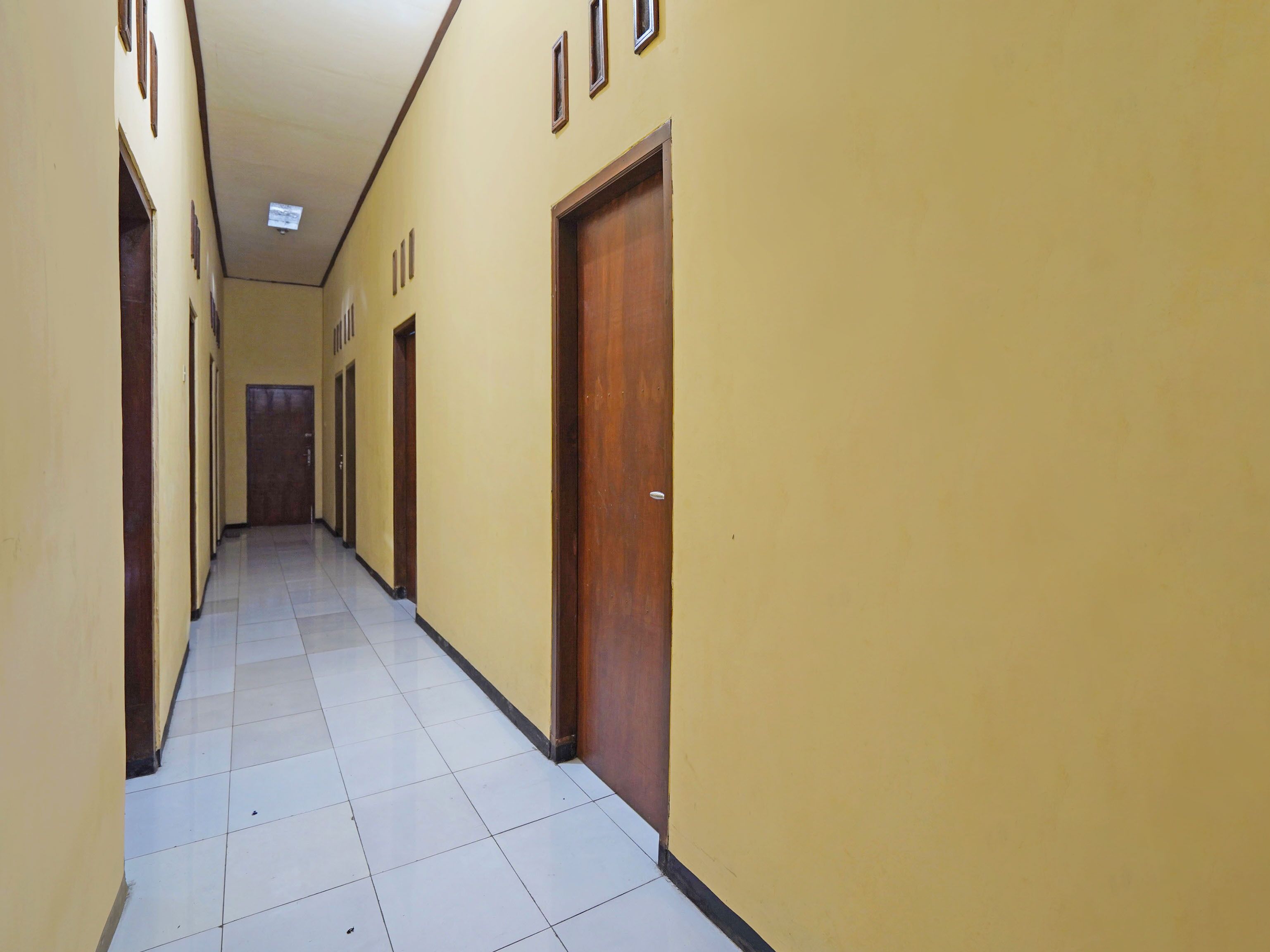 A long, narrow hallway with yellow walls and white tiled floors.