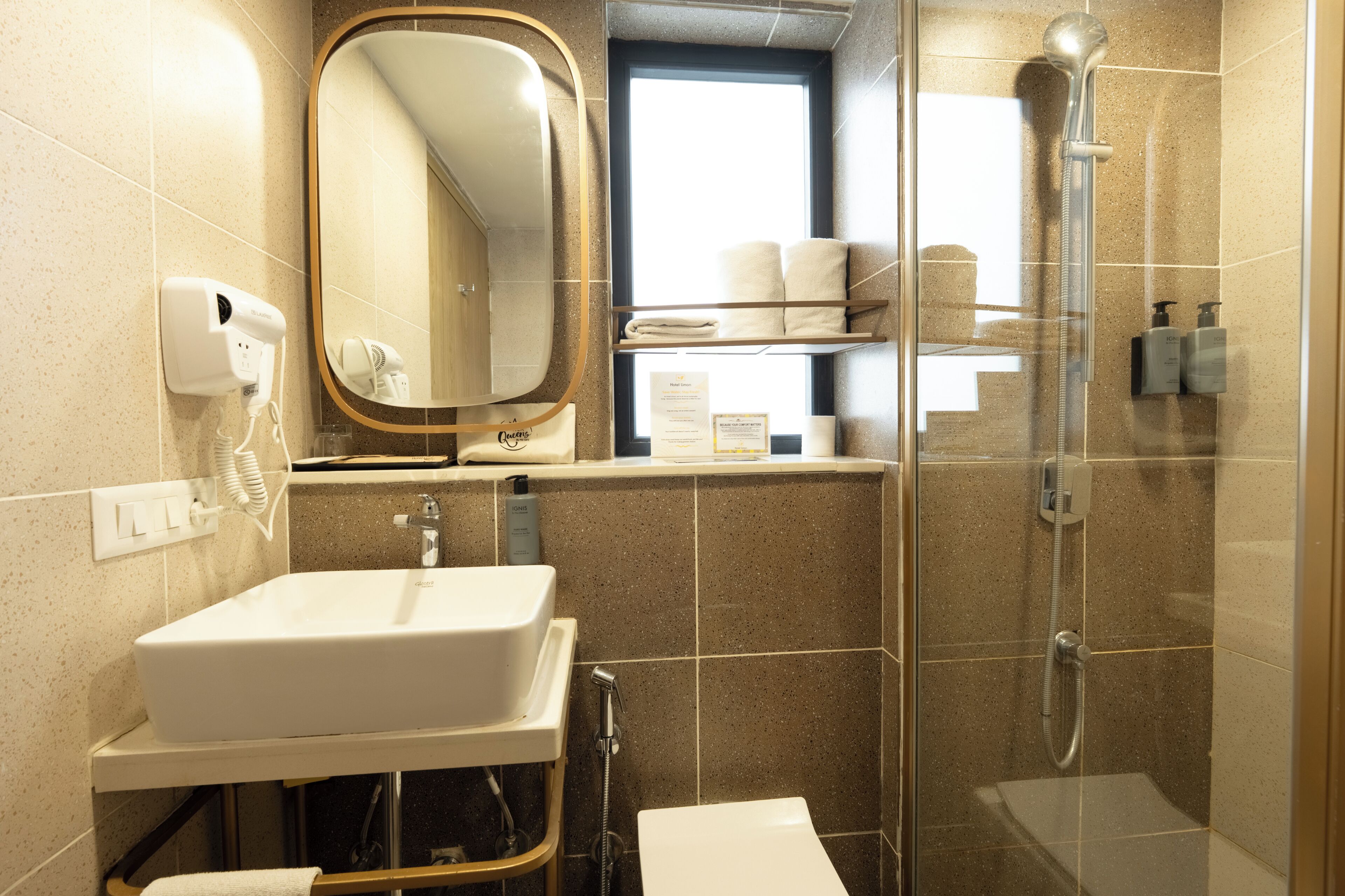 A bathroom with a sink, mirror, towel rack, shower, and a window.