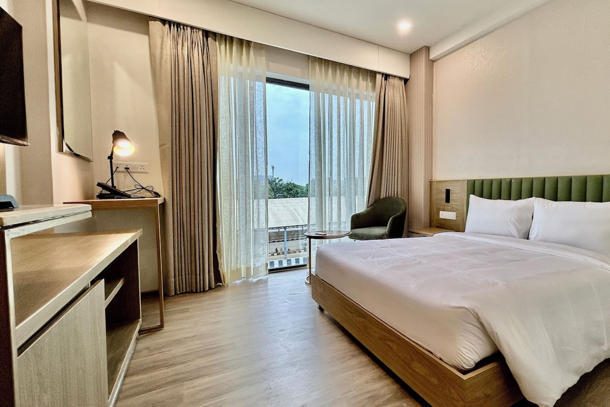 A hotel room with a bed, a desk, a chair, and a view of the outdoors.