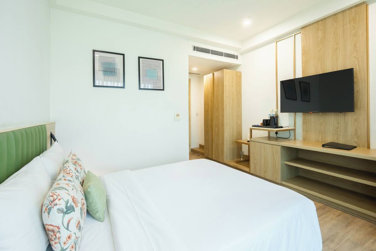 A modern hotel room with a bed, a desk, a television, and a wardrobe.