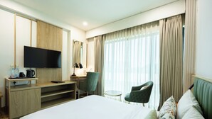 A hotel room with a bed, a desk with a flat-screen TV, a chair, a small table, and a window with curtains. - Hotel Limon Sector 29, Gurgaon (Gurugram)