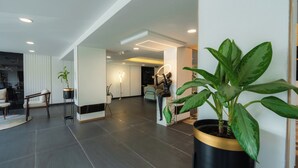 A spacious living area with a modern design, featuring a large potted plant, a seating area with a sofa and chairs, and a visible kitchen in the background. - Hotel Limon Sector 29, Gurgaon (Gurugram)