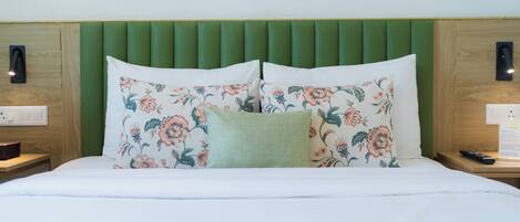 A bed with floral-patterned pillows, a green headboard, and wooden nightstands with a remote control and a power outlet.